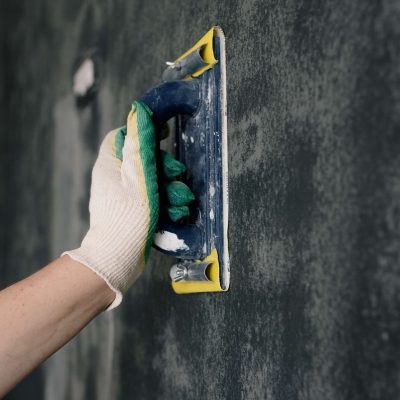 Hand with a glove sanding a wall.